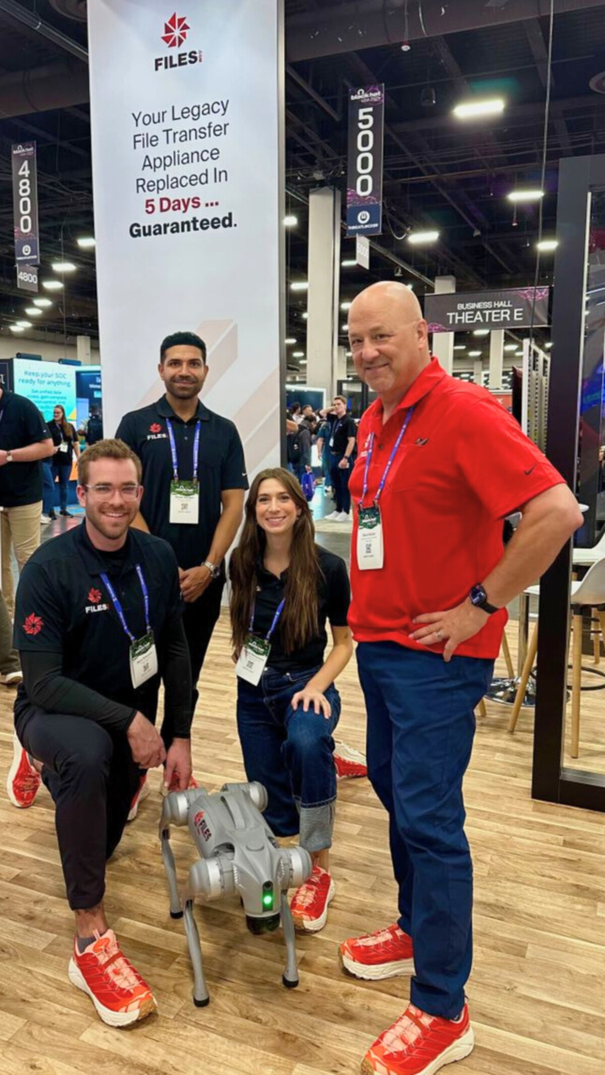 Three Files.com engineers and a colleague posed with a robot dog at an industry conference, under the company's '5 Days Guaranteed' banner.