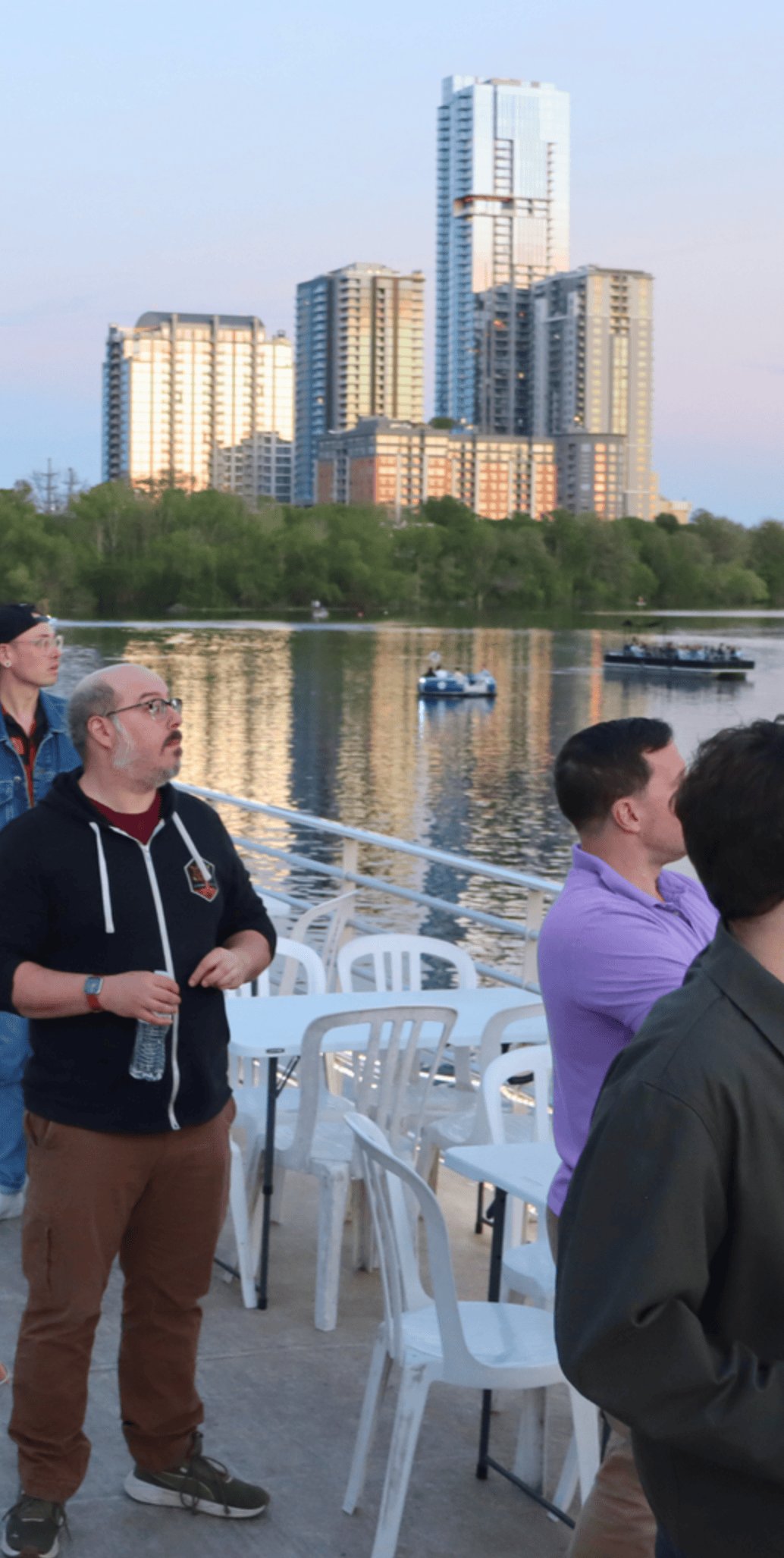 Adam on a deck overlooking Lady Bird Lake in downtown Austin at dusk, the city skyline behind him.