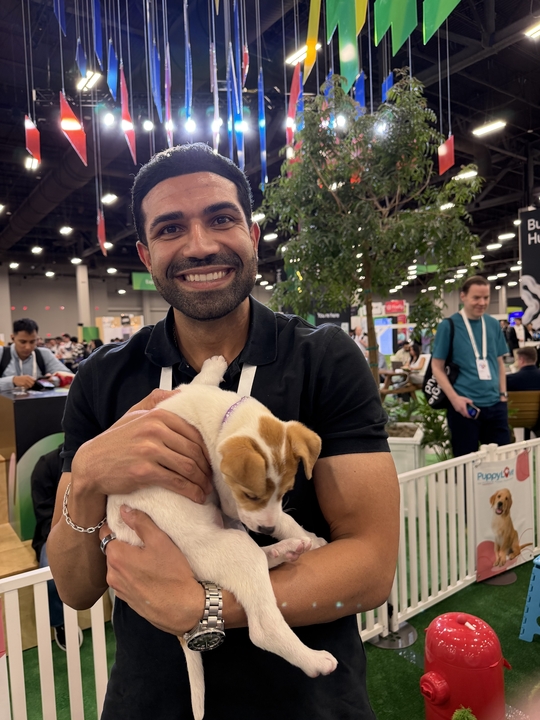 Karan smiling while holding a puppy at a conference expo floor.